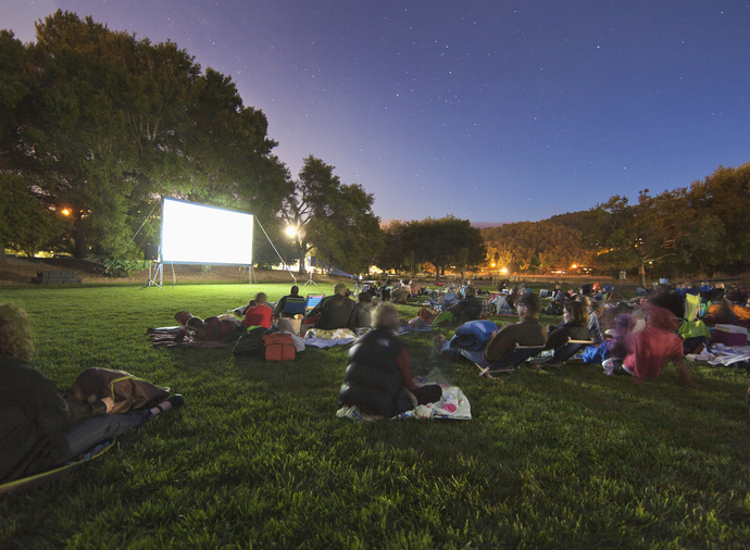 People sitting in a park in front of an illuminated projection screen