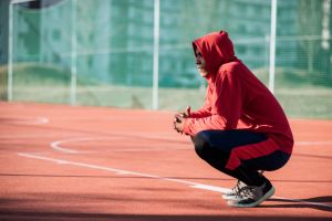 Young boy with hood on his head relaxing in urban basketball playground