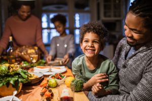Cheerful black boy with his father at dining table.