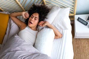 Young African American woman waking up in the morning, yawning and stretching arms in bed. Good morning.