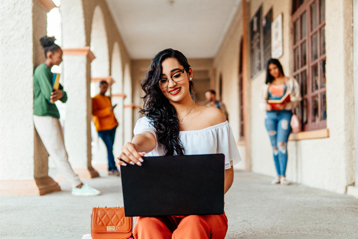 Portrait of university student sitting holding and using a laptop in a campus. Education concept.