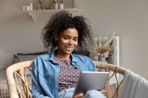 Happy young woman reading book, ebook on tablet at home