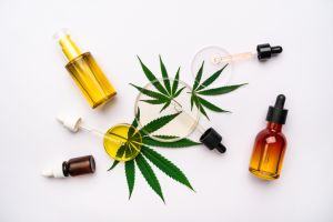 Different cosmetic glass bottles, pipettes and Petri dishes on leaves of cannabis on white background. Concept of laboratory tests about using cannabidiol and hemp oil in cosmetology and dermatology