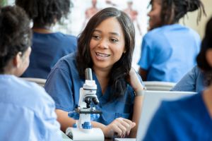 A group of medical or nursing students collaborates around a lab table with a microscope during a class.