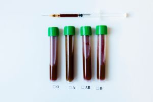 Blood test vials and syringe on a white background, labeled with blood groups O, A, AB, and B