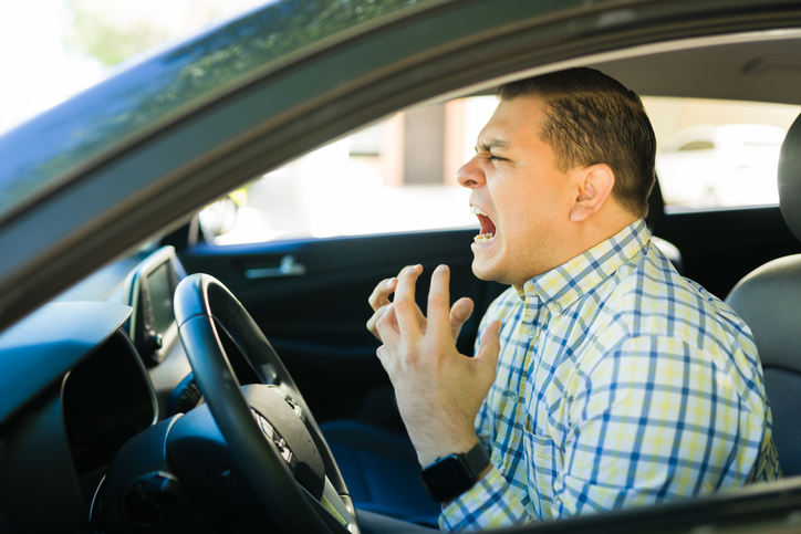 Agitated man expressing anger and frustration while driving through heavy traffic, experiencing road rage