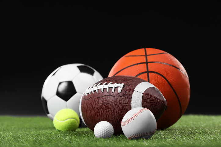Many different sports balls on green grass against black background